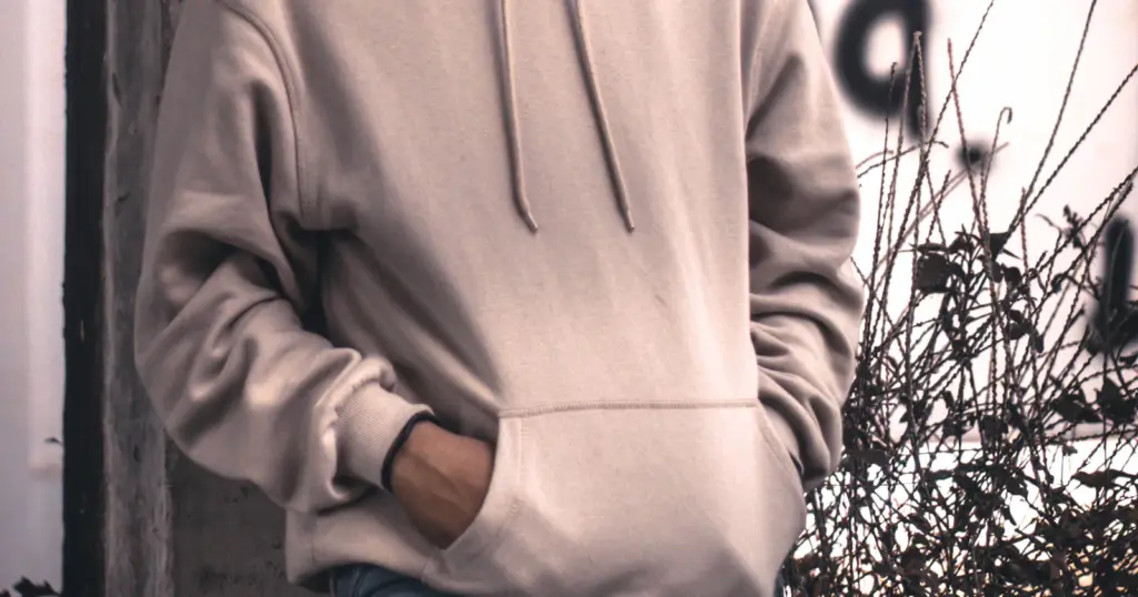 Homme en sweat à capuche gris appuyé contre un mur